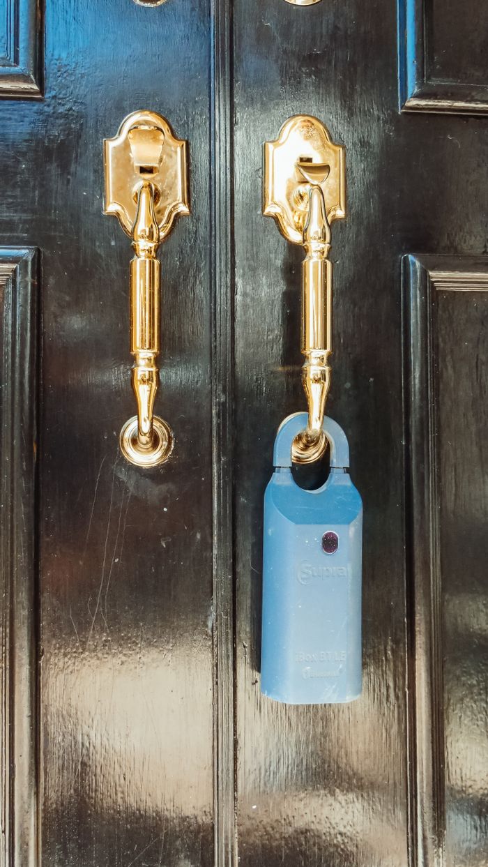 Close-up of a sleek black door with shiny brass handles and a blue lockbox, ideal for real estate security concepts.